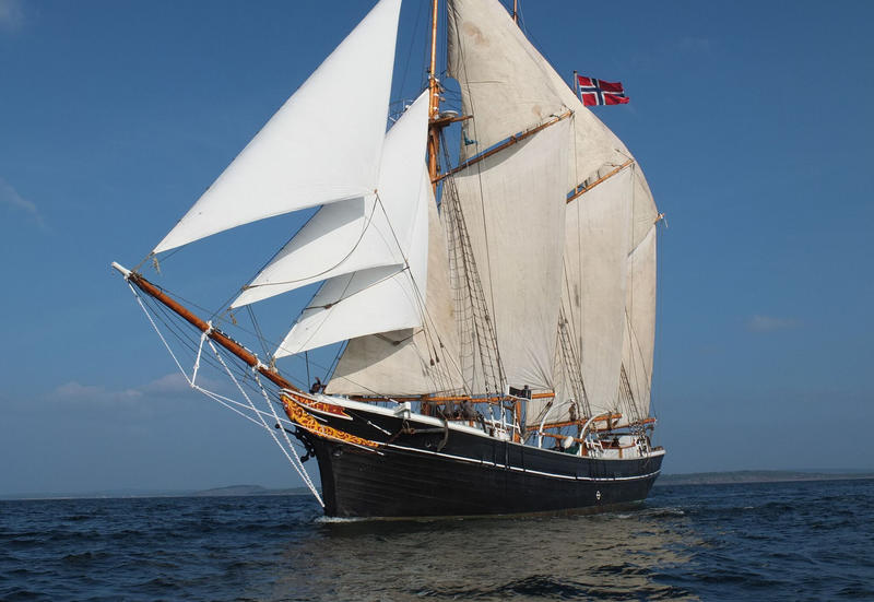 Skonnerten "Svanen" med tre master og for fulle seil ute på vannet, med norsk flagg, sett fra babord.