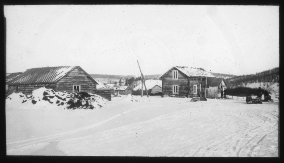 "Elvesame-hjem i Karasjok" står det på glassplaten. Boplass i Karasjok med brønnvipper på gårdsplassen.  Fotografert vinterstid.