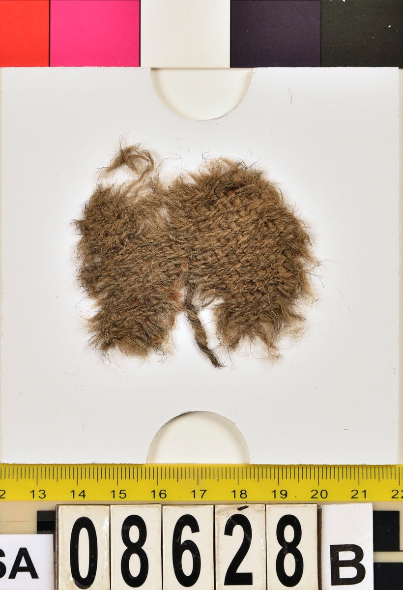 Textilfragment. 11 stycken fragment fördelade på fyndnummer 08628a-c.
Fnr 08628a består av 4 fragment av ull vävd i 2/2-kypert.
Fnr 08628b består av ett fragment av ull vävt i 2/1-kypert.
Fnr 08628c består av 6 fragment av ull vävd i tuskaft.