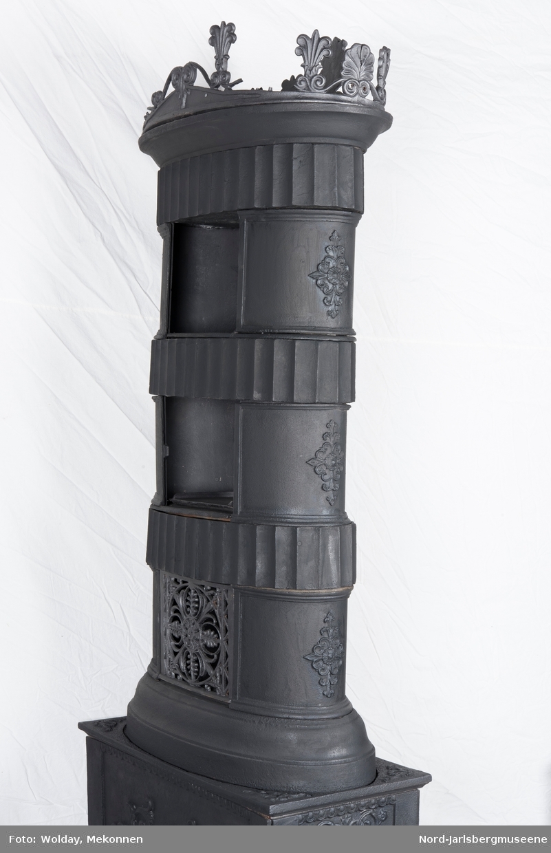 Ornamentikken som er tegnet i katalogen fra 1850, avviker noe fra ovnseksemplaret i museet. Røykkamrene på ovnen har rosettrelieff også på buet kortside, og palmettornamentet på fyrommets langside samt toppkransen avviker litt  på detaljnivå. Tverrkamrene i røyketasjene har store vertikale rifler (se anitkkens søyler).  Ovnen mangler dør, over døråpning et firedelt rokailleornament i flatt relieff.Toppkrans med palmetter og rokokkosnurrer.