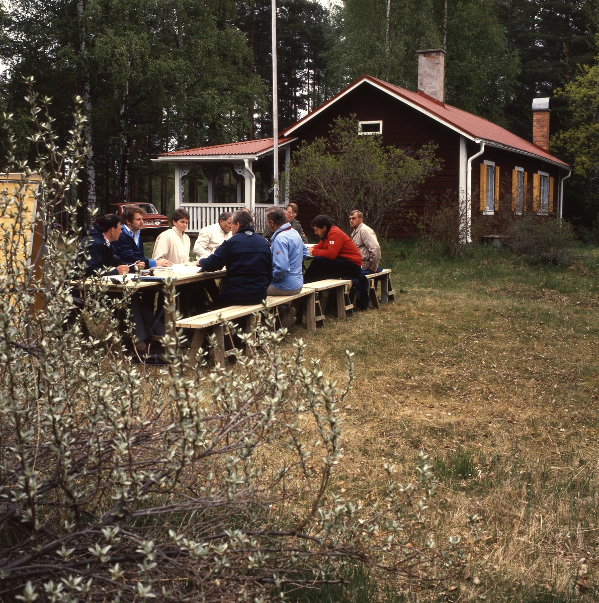 En grupp män sitter runt ett bord utanför Albert Vikstens  torp vid Ängratörn.