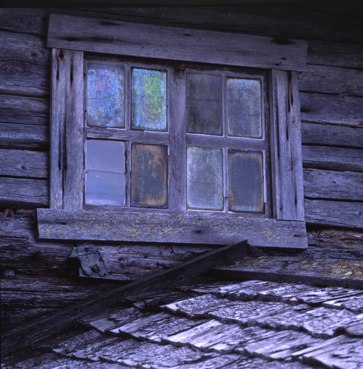 Fönster på en fäbod. Fönterspröjsen är av trä och rutornas glas har förändrats genom åren och skiftar i olika nyanser. Här syns också en del av takspånen. Färilaby väster om Ängratörn i Degerkölsvallen, 3 till 4 september 1991.
