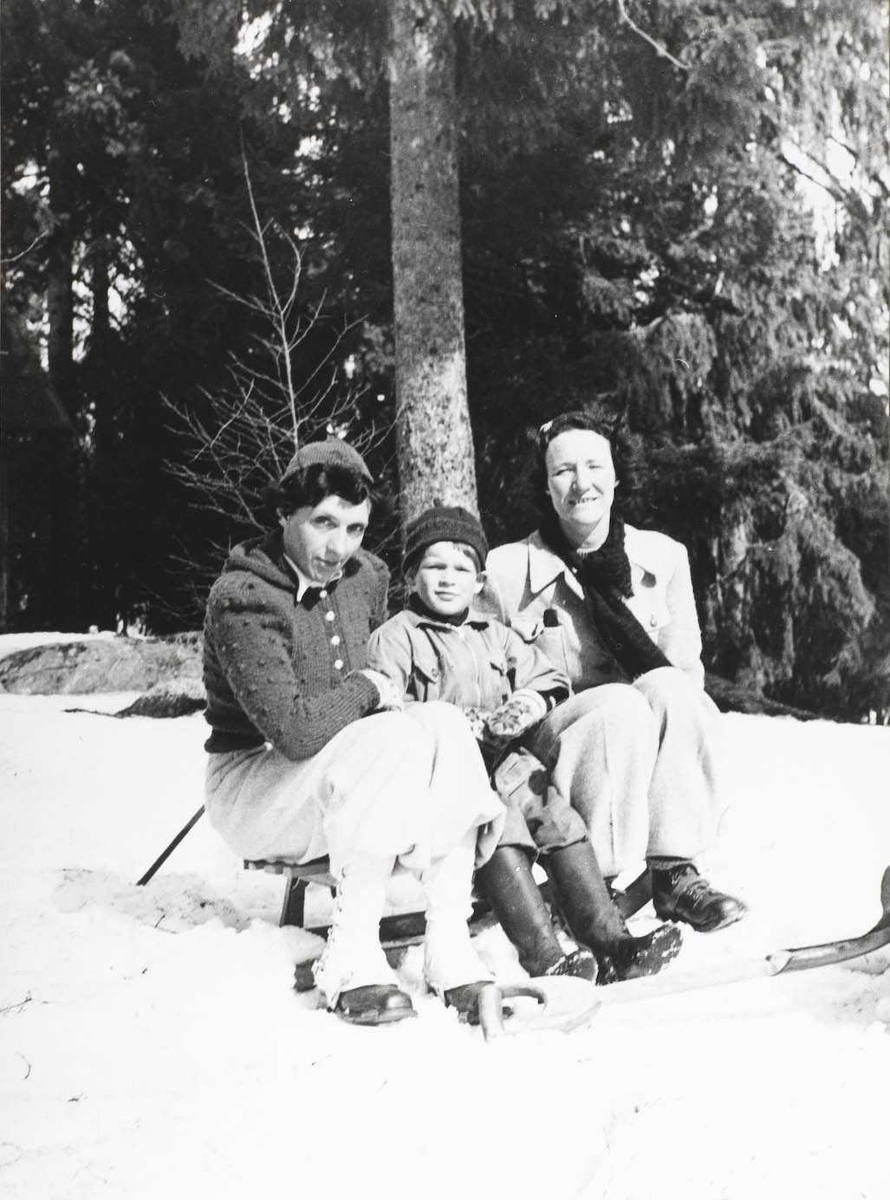 To damer og en liten gutt sittende i snøen.