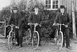 Postkort av tre herrer på sykkel utenfor våningshuset på Bøh