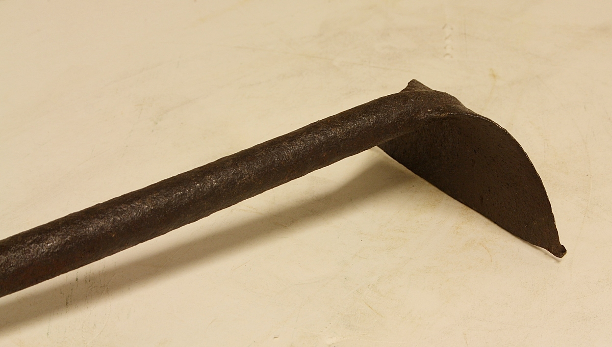 Grovt tilvirket treskaft. Langt metallskaft festet med to store spiker/nagler til treskaftet. Vifteformet, trekantet blad.