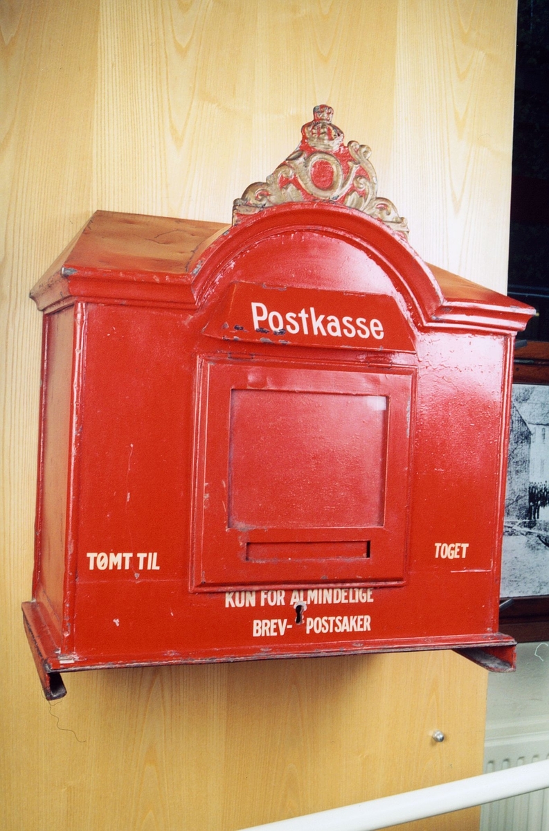 Rødmalt postkasse med tekst og logo over buet topp.