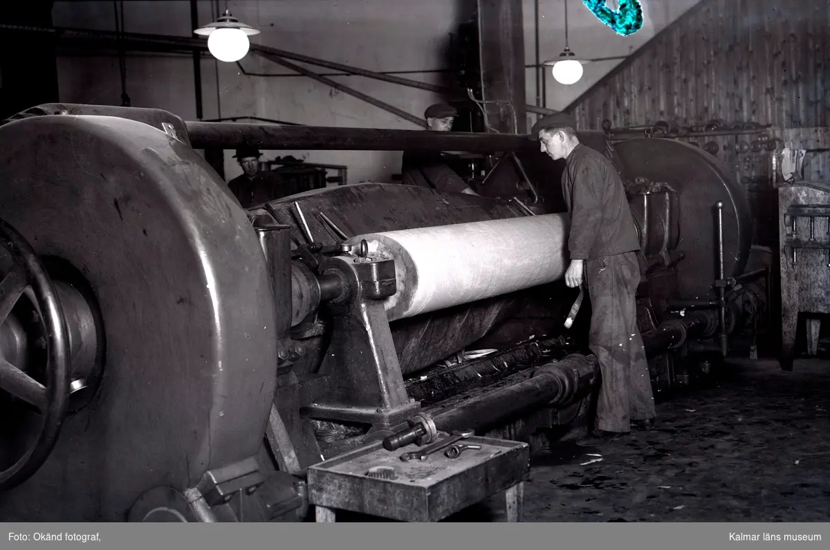 Personer som arbetar vid en maskin som svarvar fanner ur en stock. Bohman & Johanssons fanérfabrik, Blomstermåla.