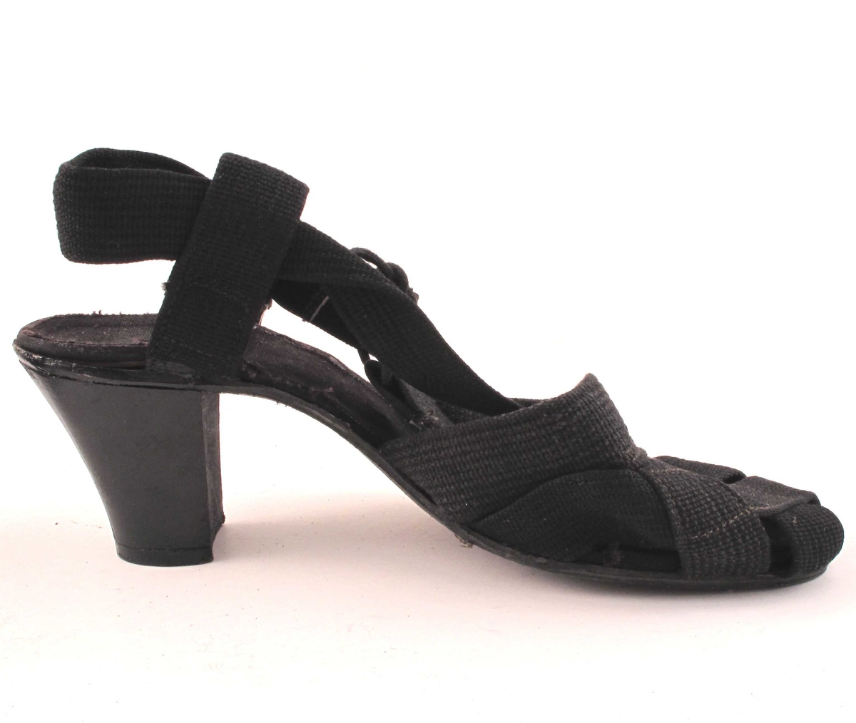 Et par høyhælte sorte damesko i tekstil.  Importerte.  Lukter svært sterkt av organsk lim, ukjent type.

Skoene har trehæler, men sålene er bygd opp av tekstil over lær eller hard gummi.  Såle stiftet fast under hælen.

Størrelse 4

"Overlæret" er laget av flettde og sammensydde sorte bånd, som fortsetter ut i lengre bånd rundt hælen.  Haælbåndet er festet til sålen med stropper på begge sider av hælen.  Lisseknyting på utsiden av vristen.