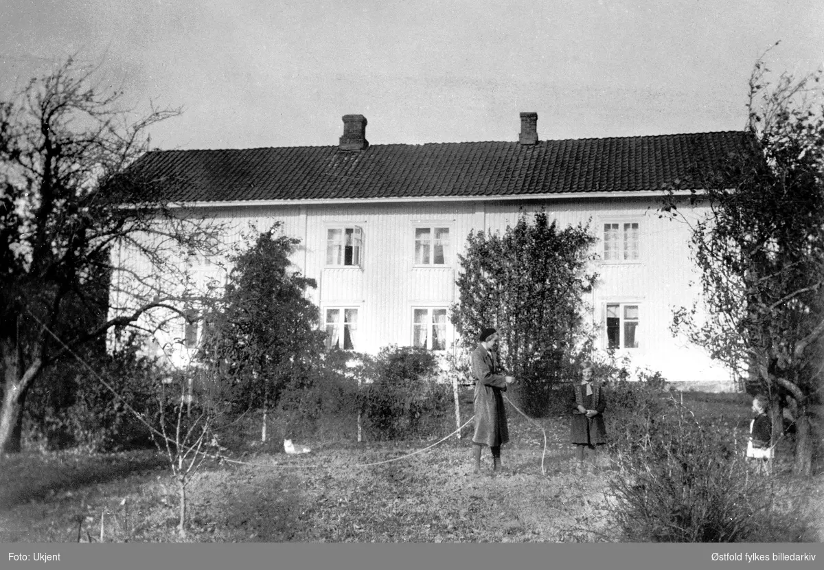 Våningshuset på gården Kjos 70/1 i SKiptvet i 1932. Tre personer i hagen er ukjente. Våningshuset sett fra hagen og syd.
