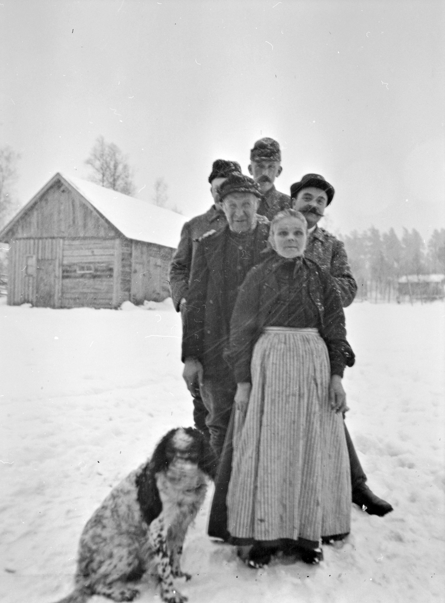 En kvinna, fyra män och en hund vid Hagalund, Västra Jära Södergård, Hjalmar Bauers arrendeställe. Närmast står Johan Svensson "Sågarn" och hans hustru Lolla. Mannen längst till vänster är skogvaktare.