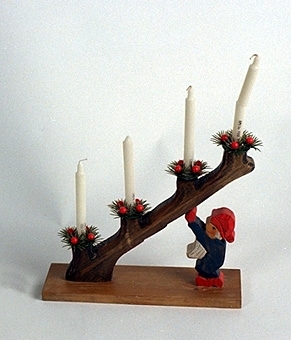 Julljusstake av trä. En gren med fyra ljushållare hålls av en tomte.
Fyra stearinljus och ljusmanschetter av plast.