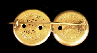 Broschen är tillverkad av två mässingsknappar som varit uniformsknappar för järnvägspersonal.
Ekelöf tjänstgjorde på järnvägssträckan Skara-Lugnås.
Tillverkarna är tillverkarna av knapparna, inte broschen.
Se bilaga