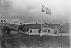 Bolighus, gjerde, flaggstang m/flagg, stabbur.