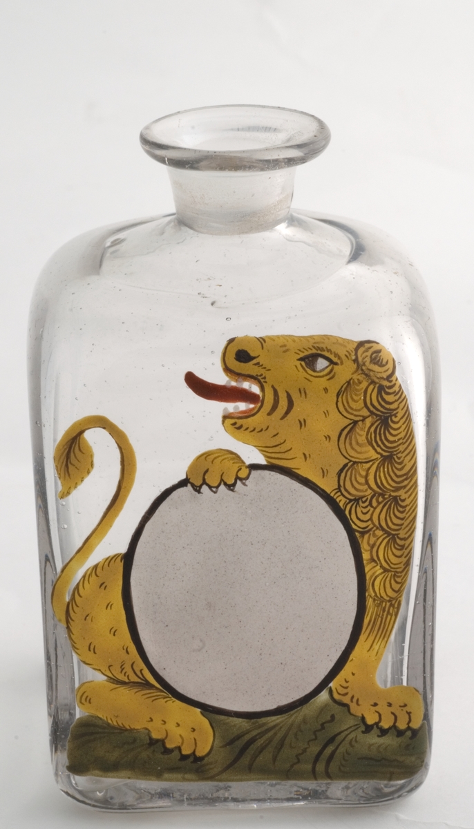 Firkantet standglass uten propp. Trang hals.  Påmalt ovalt hvitt etikettfelt. Dekormotiv: gul løve som holder etiketten.
