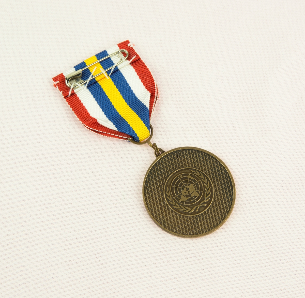 Medalj, på framsidan stansad med text: Naqouramarschen Swedlog. I mitten av medaljen frinns det Libanesiska trädet samt de tre svenska kronorna. Baksida av medaljen är stansad med FörentaNationernas (FN) loggotyp. Bandet består av 7st färgade fält: Det mittersta är gult, om det två blåa fält som sedan är följt av ett vitt och ett rött fält om vardera sida.