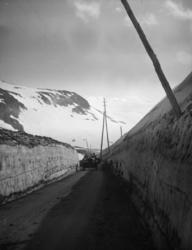 En bil på veg mellom høye brøytekanter på Strynsfjellet.