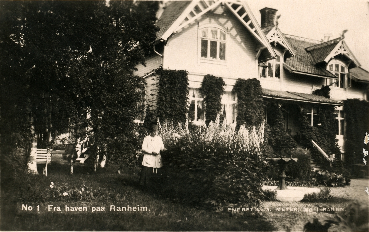 Prospektkort. Hagen på Ranheim. Kvinne står i frodig hage foran trehus i sveitserstil. Villaen ble bygget av L. A Meyer i 1902.