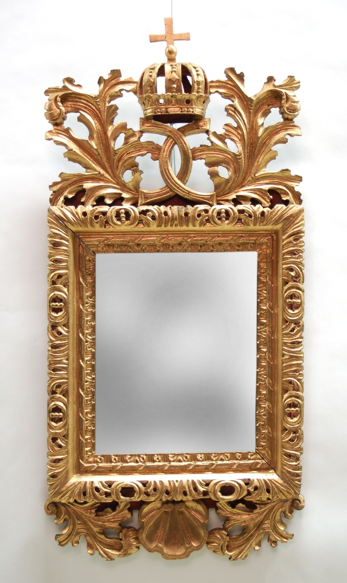 Spegel, barock, ramen rikt skulpterad, växtornamentik m.m. samt förgyllt. Överst kunglig krona och spegelmonogram.
Träet är på baksidan rött.