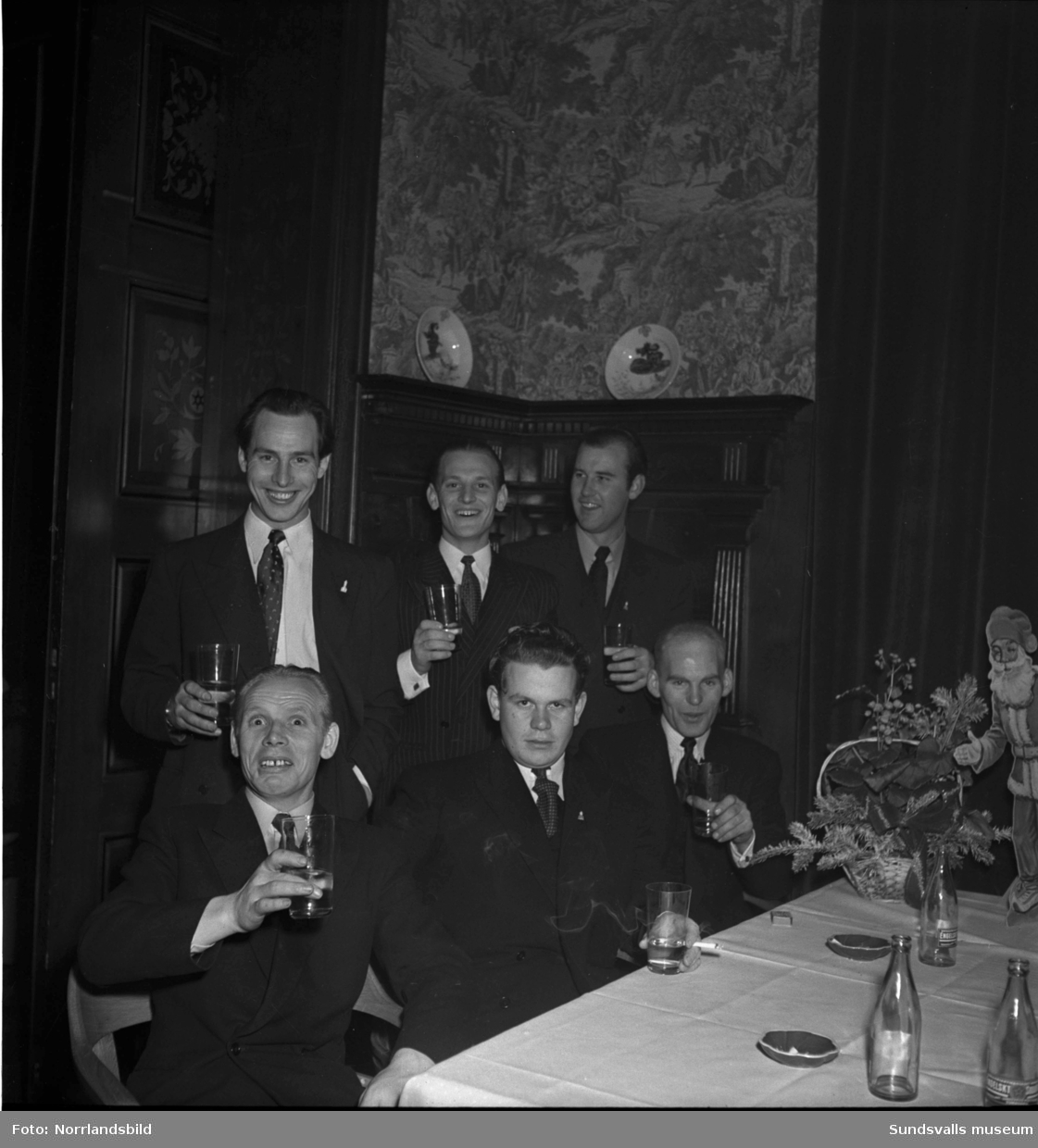 En festkväll på Knaust. Damer i vackra klänningar och varsin blombukett samt en gruppbild med sex glada herrar som ser ut att utbringa en skål.