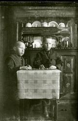 To gutar sit ved eit bord og spelar spel. Olmhusskåpet i bak