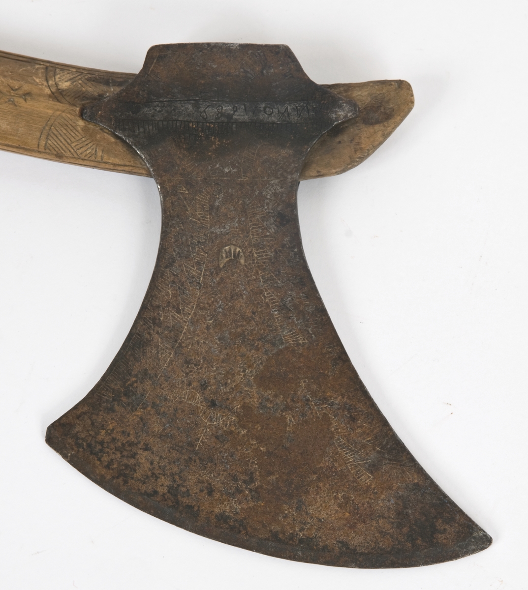 Asymmetrisk blad med lang øvre spiss og kortere nedre spiss. Bladet er klieformet. med påsmidd egg- Øksen har stset dekor på begge sider. Skjellmønstet smedmerke på utsiden. Øksen er datert 1689.
Øksehammeren har skaftehull og fliker.
Gammelt skaft med dølle,pigg.og 2 oppsmidde fliker.
Skaftet er krummet og merket med navn og datert 1688. Skftet er noe avkortet.