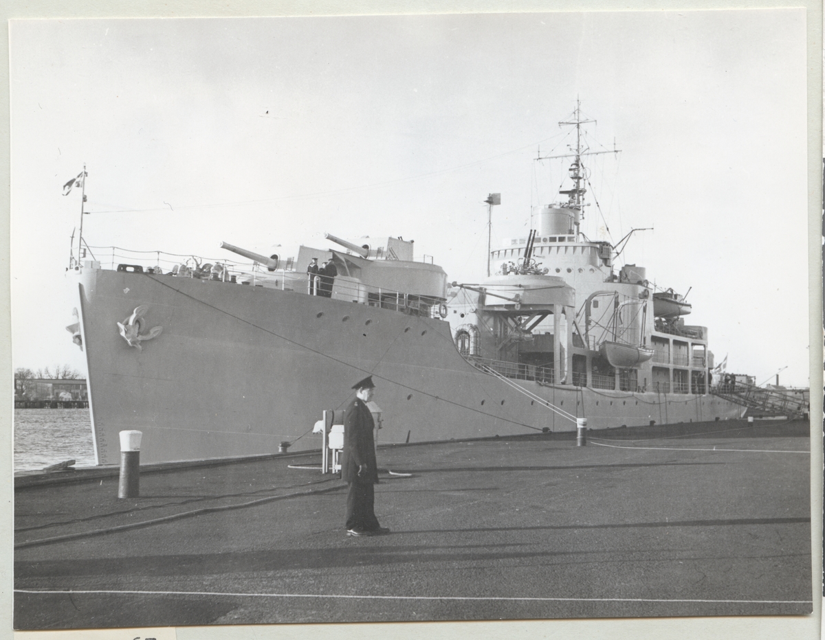 Bilden visar minfartyget Älvsnabben från babordssida framifrån som ligger förtöjt i hamnen. I förgrunden står en ensam marinsoldat på kajen.