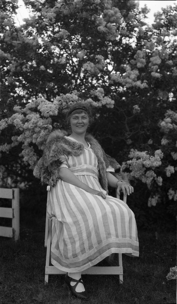 Kvinne som sitter foran en syrinbusk. Trolig Gudrun Hveem, gift med Johannes P. Hveem på Hveem mellom i Østre Toten.