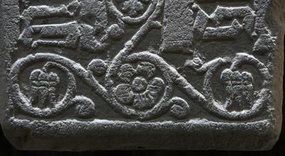 Detalj fra en middelaldergravstein; en flott uthugget fembladet blomst med bladranker rundt.