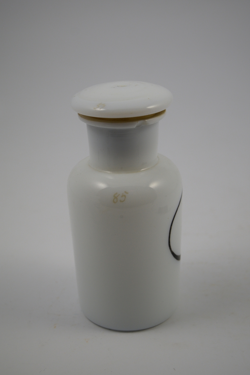 Porselenskrukke med propp. Sort oval etikett påført på krukken. Til oppbevaring av legemidler/pulver.