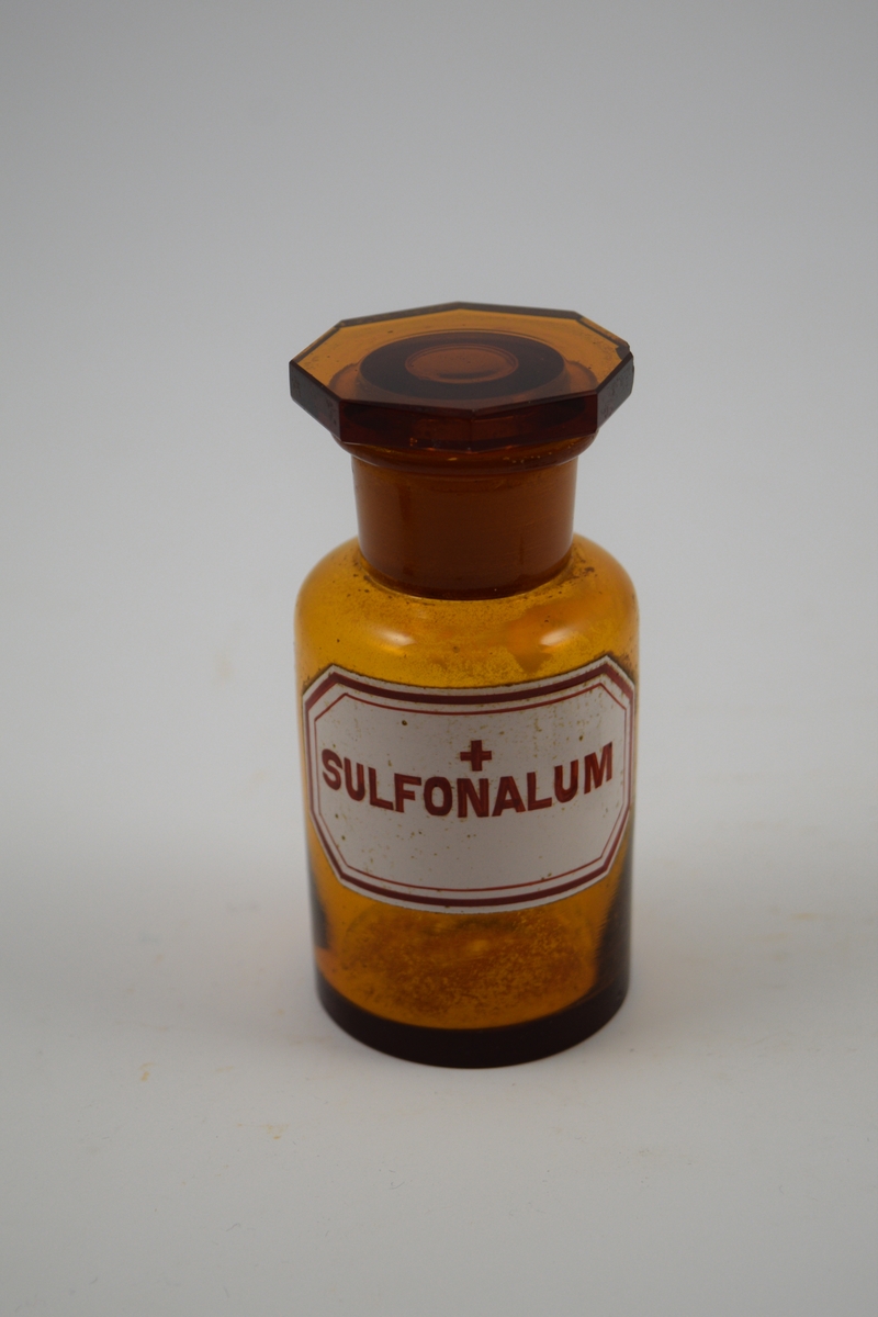 Brun glasskrukke med glassporpp. Etikett hvit med rød skrift, ett kors, betyr at innholdet er giftig. Har inneholdt Sulfonalum. Sulfonal ble brukt som sovemiddel, syntetisk, ettkorsgift.