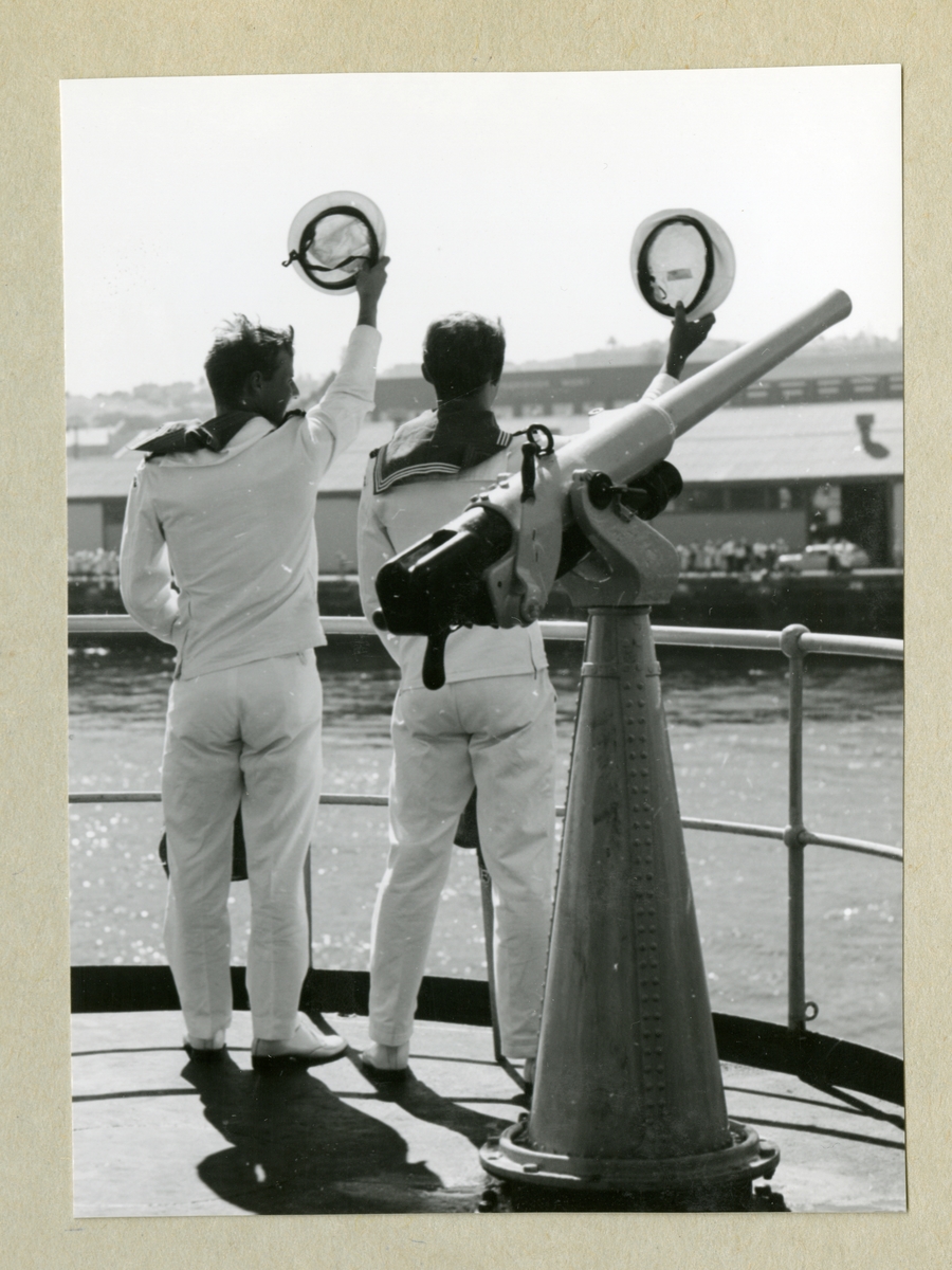 Bilden föreställer två uniformsklädda besättningsmän ombord på minfartyget Älvsnabben som vinkar adjö till hamnbesökare under långresan 1966-1967.