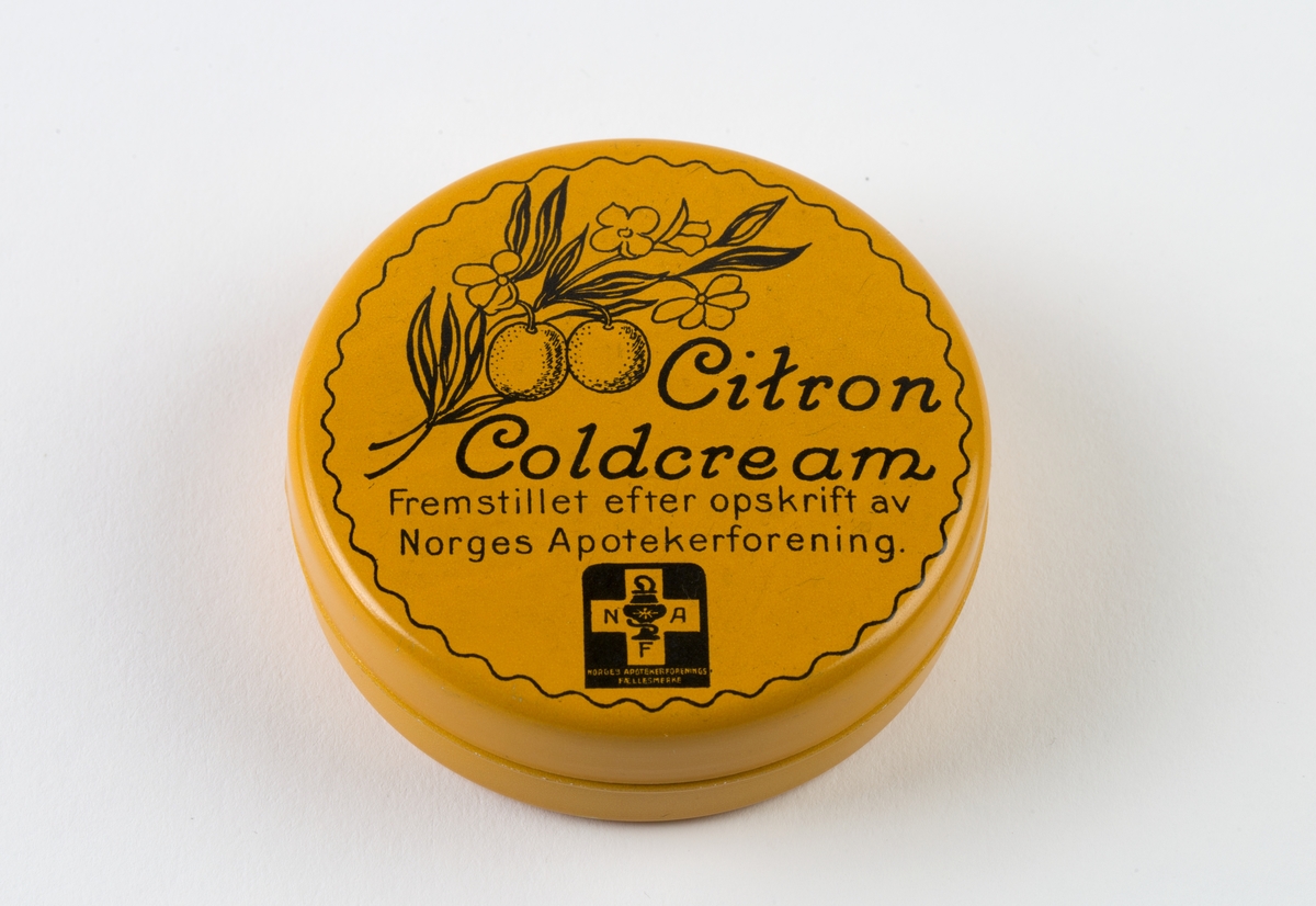 Rund salveeskemed bunn og lokk. Lokket er påtegnet en kvist fra citrontre, innhold og logo for Norges Apotekerforening.