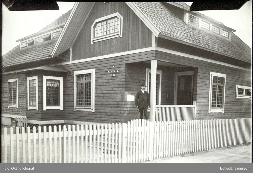 En man står på en veranda på ett stort hus med staket runt om ...