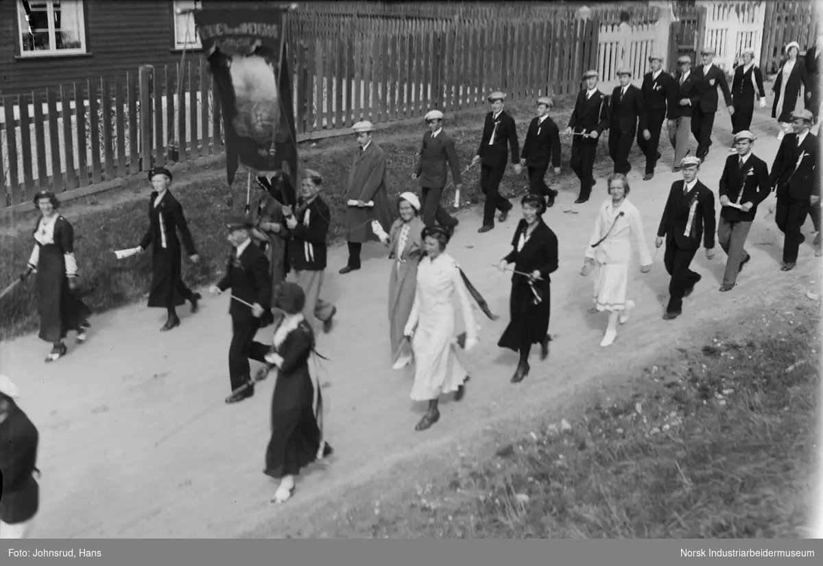 17. mai feiring 1933. Russen med russelue og russestokk marsjer langs gate med skolefane.