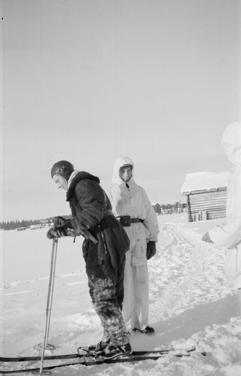 Två vinterklädda män tillhörande Svenska frivilligkåren i Finland, F 19. Den ena mannen står på skidor.