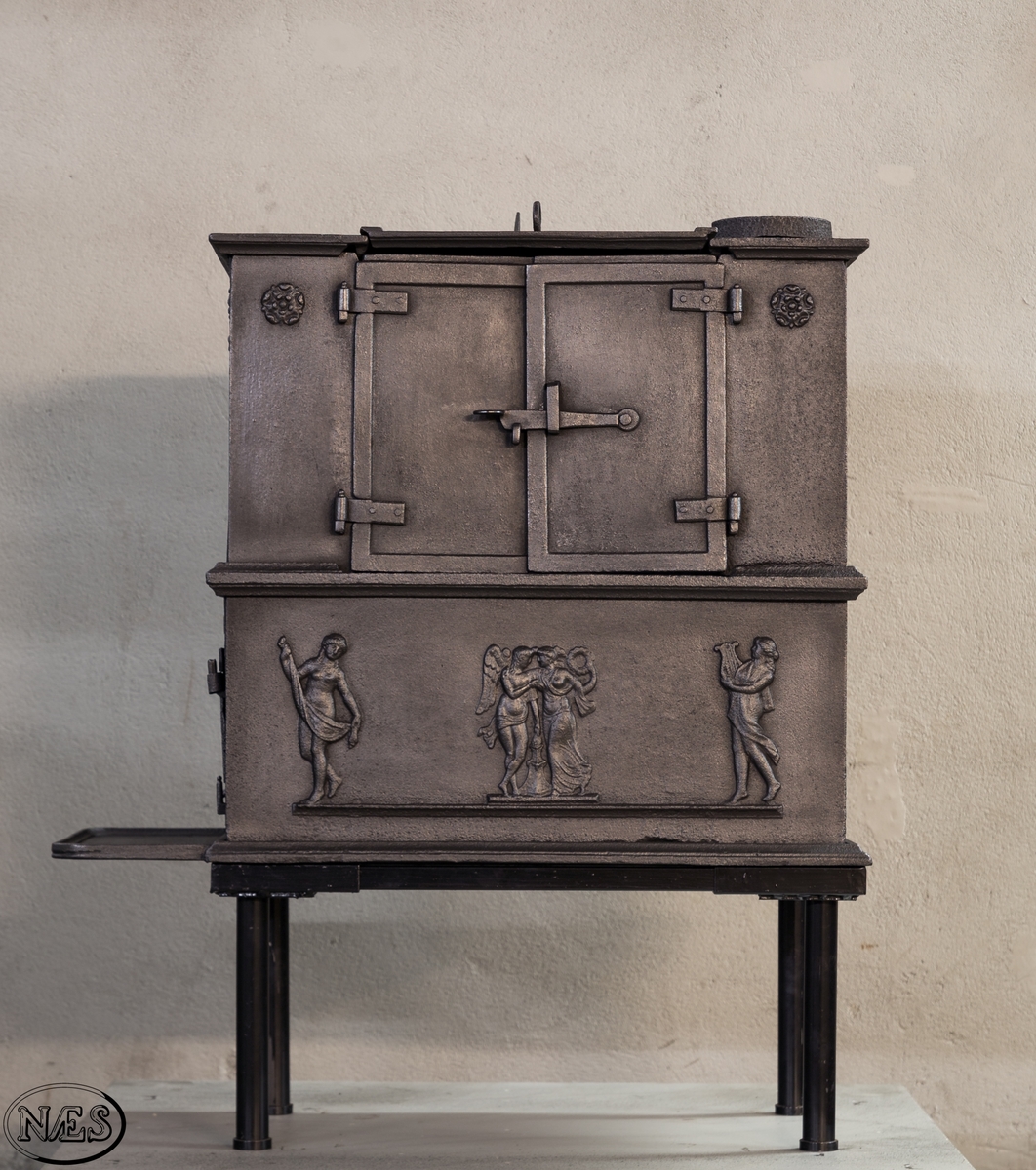 Kokeovn i to etasjer med eget fyrkammer og kokerom. Kokerommet kan åpnes med to dører på langsiden og med en luke i topplaten. Ovnsdøren til fyrkammeret er på kortsiden 1 etg. På langsidene i 1. etg er det tre muser og en engel med lette draperier på en enkel profillist. På kortsidene 2. etg er det draperikledd dansende muse på enkel profillist med en rosett i hvert øvre hjørne. Langsidene i 2.etg er dekorert med en rosett i hvert øvre hjørne.