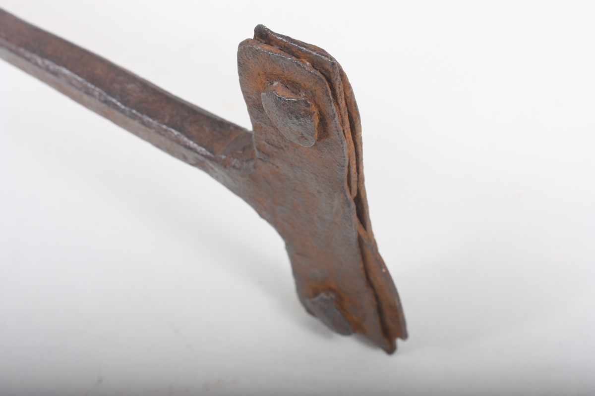 T-forma firkantjern med tverrståande handtak i øvre enden. I nedre ende er jernet splitta og det er nagla fast jern i splitten. Ukjent kva det har vore nytta til.