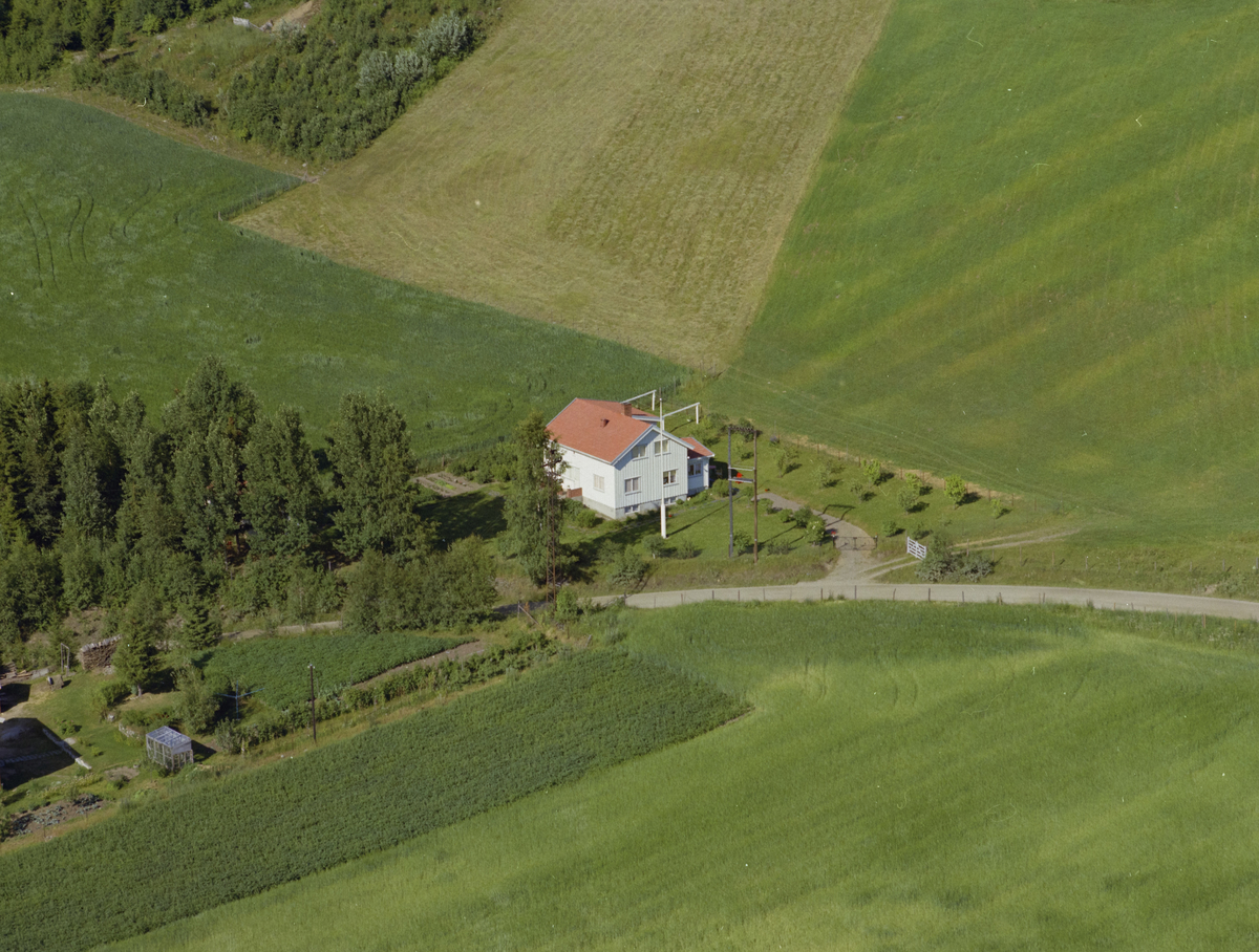 Øyer, Tretten. Hvitt ett og ethalvtetasjes hus, kjøkkenhage, flaggstang omgitt av dyrket mark på østiden. Et skogholt til venstre på bildet, Sør-Trettenvegen midt på bildet.