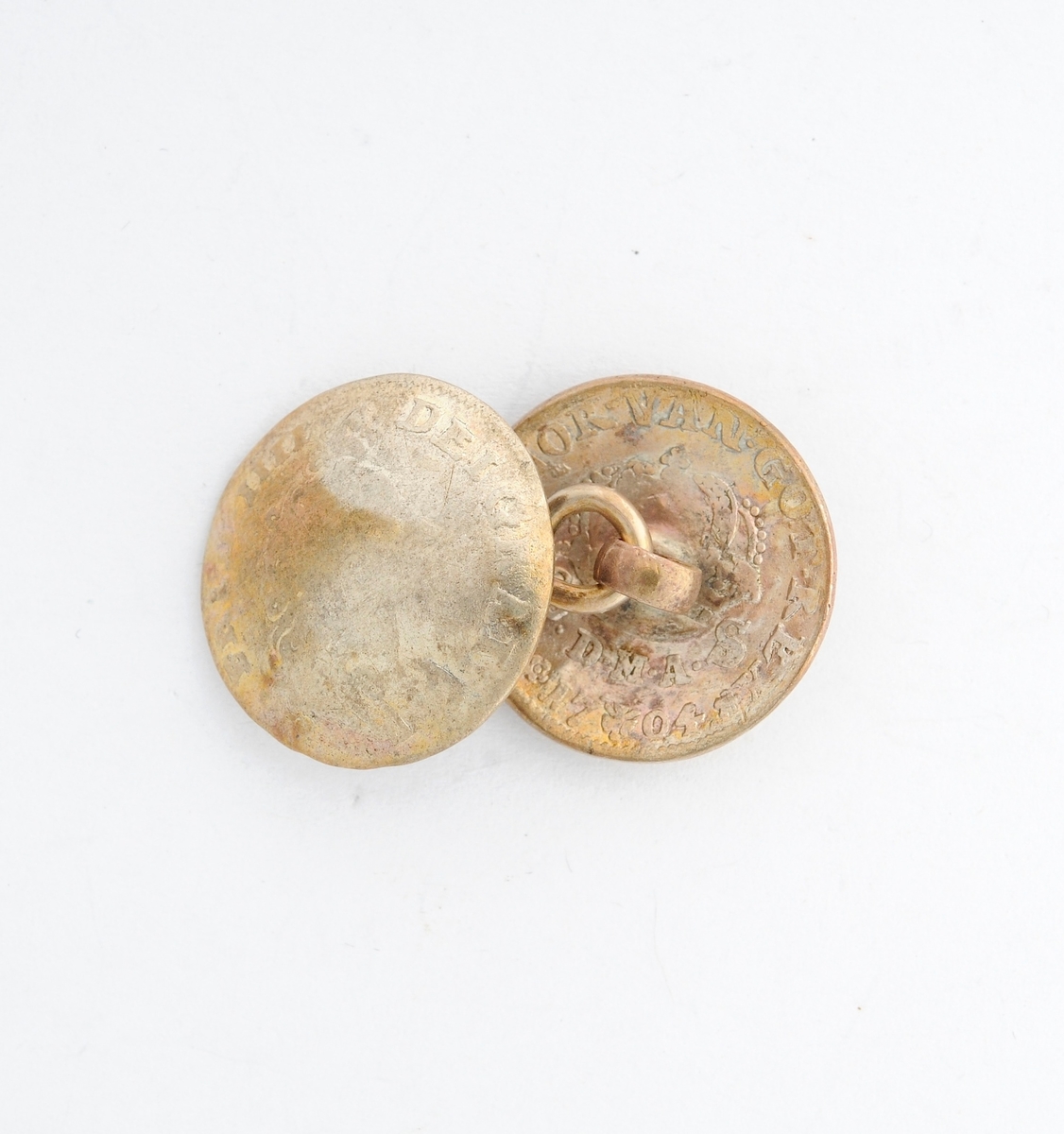 Sølje, halsknapp i sølv. Sett saman av to knappar i ei åttetallsforma hempe i messing. Knappane er gamle myntar frå 1702 og 1704, og som er laga om til knappar. (sjå nærmare registrering på arkivkort 7144).