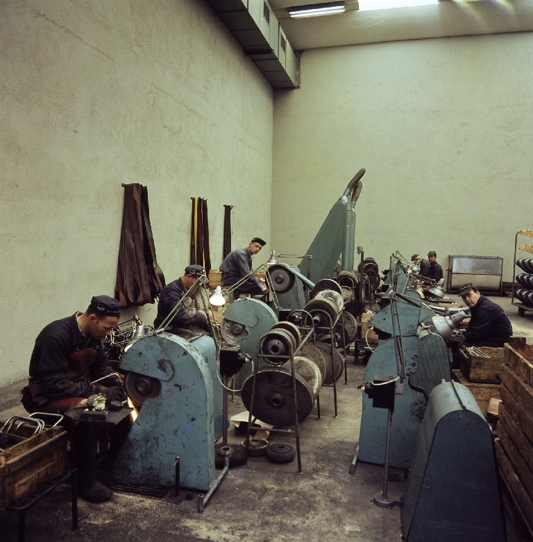 Arbeidere sitter ved slipemaskiner og sliper deler før lakkering og fornikling i sliperiet i bygningen "Nr. 11" til sykkelfabrikken til Jonas Øglænd AS på Sandnes.