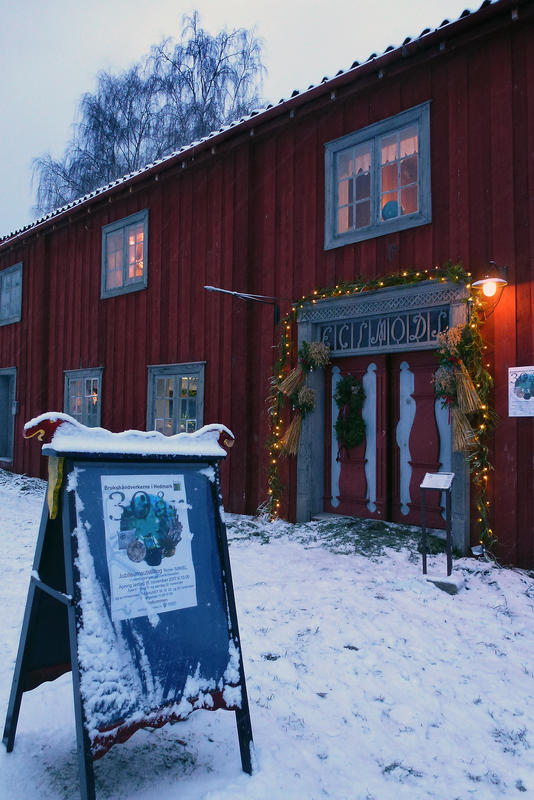 Inngangspartiet til et gammelt, rødt hus er omgitt av en lyslenke, foran står en reklamebukk med plakat om åpningstider. (Foto/Photo)