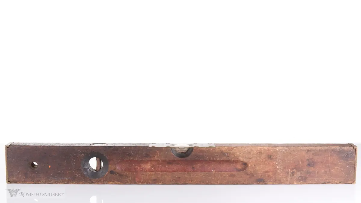 Rektangulær trevater med topp- og endeplater i messing og to bobler. Ovalt utfreset spor på begge sider av vateren. Gjennomgående opphengshull.