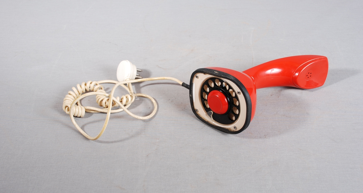 Analog bordtelefon med tallskive og av/på knapp i bunnen. Mikrofon og høyttaler i ett stykke. Spiralledning med trepinns kontakt.