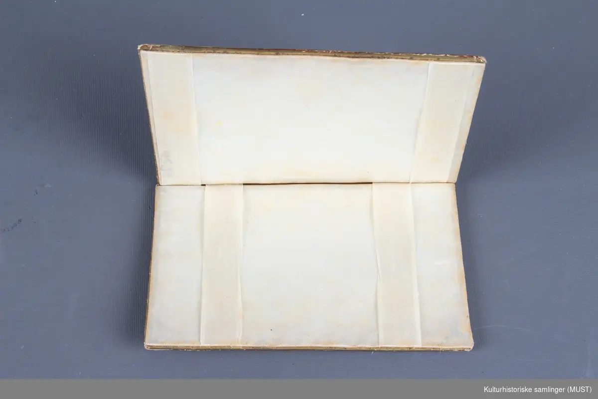 Visittkortmappe av papp. Permene består av hvit, perforert pappkartong og hvit silke. På permene korsstings- og perlebroderier, langs kanten en "gullist".