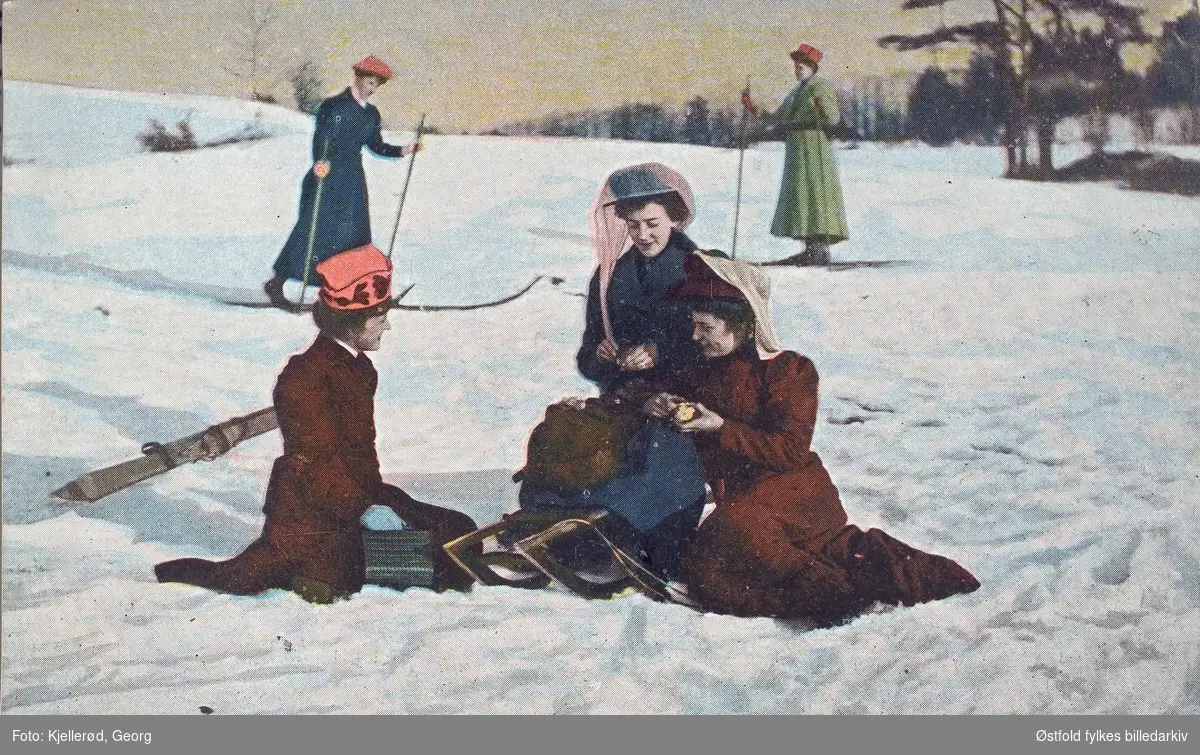 Postkort, kolorert lystrykk kvinner som går på ski og aker, rast i bakken. Poststemplet 1910.