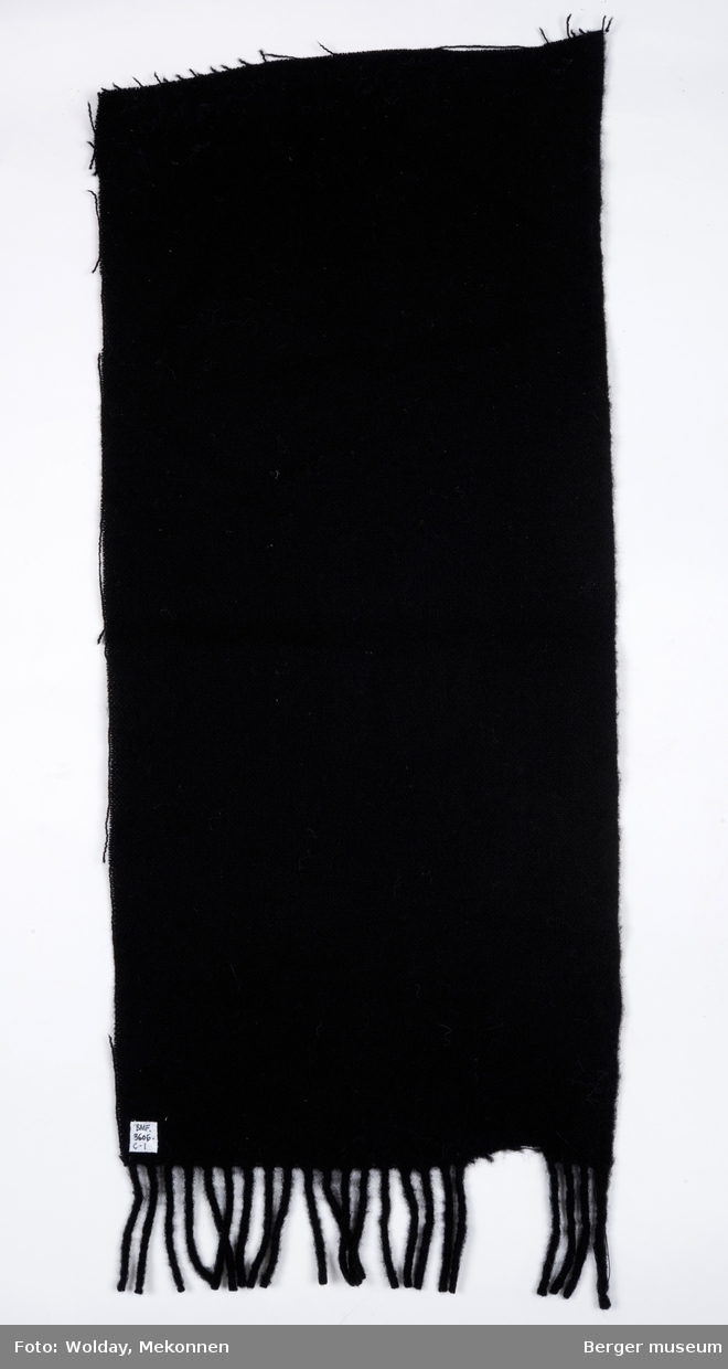 Ensfarget tekstilbit, med klippete kanter, ene kortside med frynser.