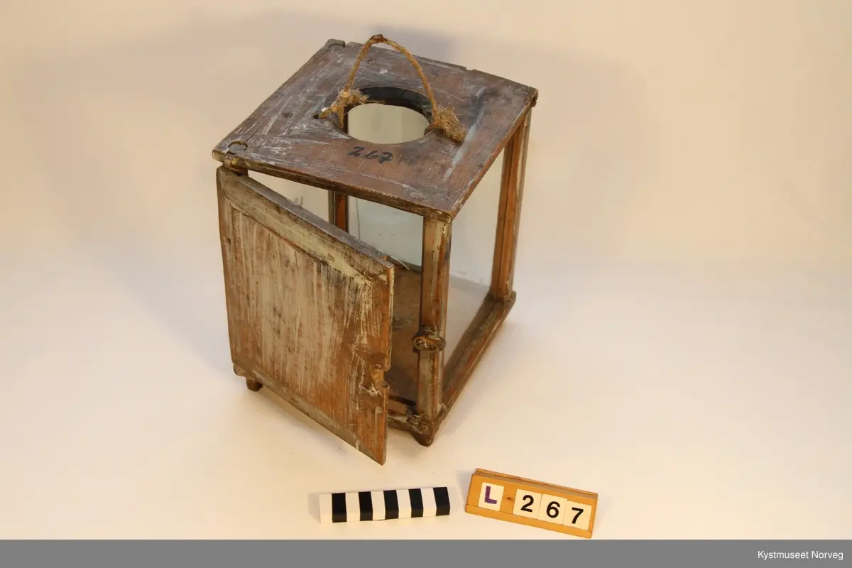 Lykt i tre med glassvegger og tredør. Lykta er rektangulær, og har tre vegger av glass og tredør. I bunnplata er det innfelt et metallfeste for talglyset. I toppen er det laget åpning for varme og røyk fra lyset. I tillegg er det laget to hull i lokket for feste av tauhåndtak. Hjørnene har trestykker, hvor det er laget spor for innsetting av glasset. Likeså topp og bunnplate. Døra låses av med en lite trestykke som kan vrides.