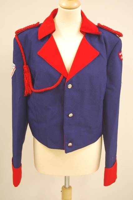 Jakke (a): blå polyester med for av blå kunstsilke. Rød krage og slag og oppslag på ermene. 3 blanke knapper. Røde epauletter med blanke knapper, rød pyntesnor rundt høre arm
Bukse (b): blå polyester, røde render i sidesømmene. Nylon glidelås i gylfen. 1 svart knapp
Magebelte (c), rødt, blankt kunstfiberstoff, foret med rød bomull. 3 folder midt på. Lukkes med borrelås. 91 l, 11.5 b
Pyntesløyfe (d), samme tøy som beltet. Røde frynser i nedkant. Kan festes med borrelås til belte. Todelt. 49 l, 12 b.