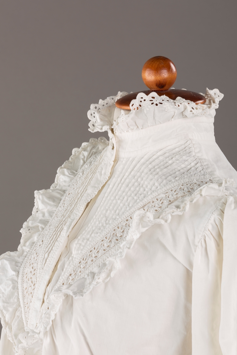 Form: Lange ermer, fotsid.

Blondekant og rysjer i halsåpning.
To knapper i metall kledd i tekstil. Mangler en knapp.