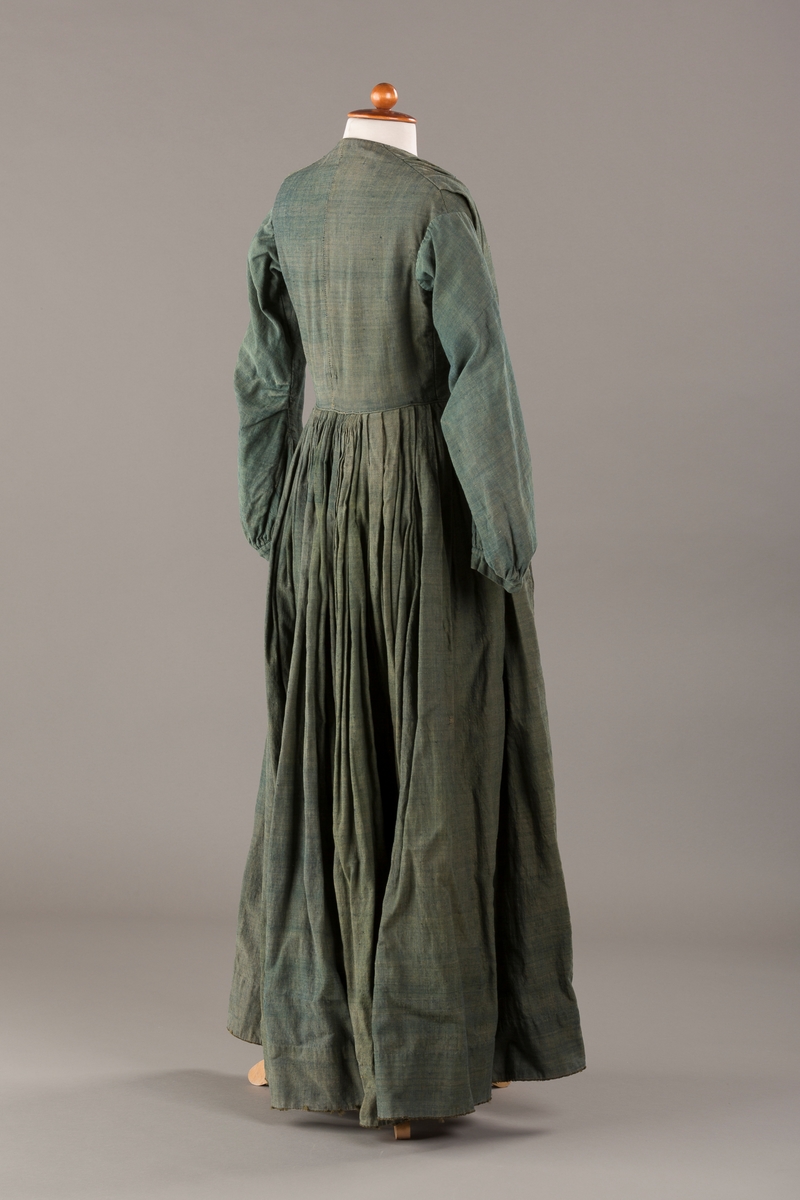 Form: Trangt liv med legg foran, skjørtet sydd med legg i livet.  God vidde i skjørtet, lange armer. Fem hekter i livet mangler.